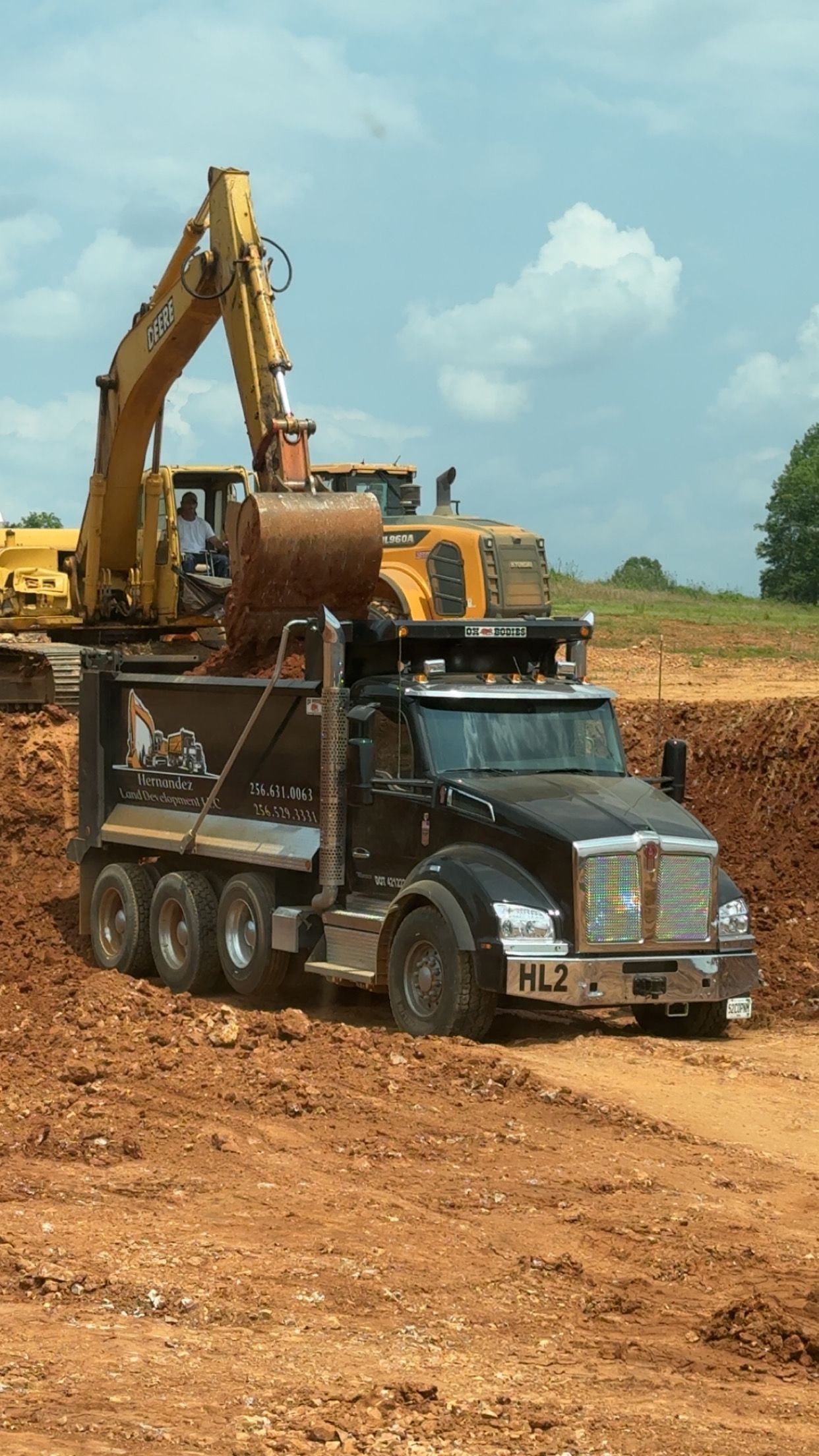 A dump truck is driving through a dirt field next to an excavator.