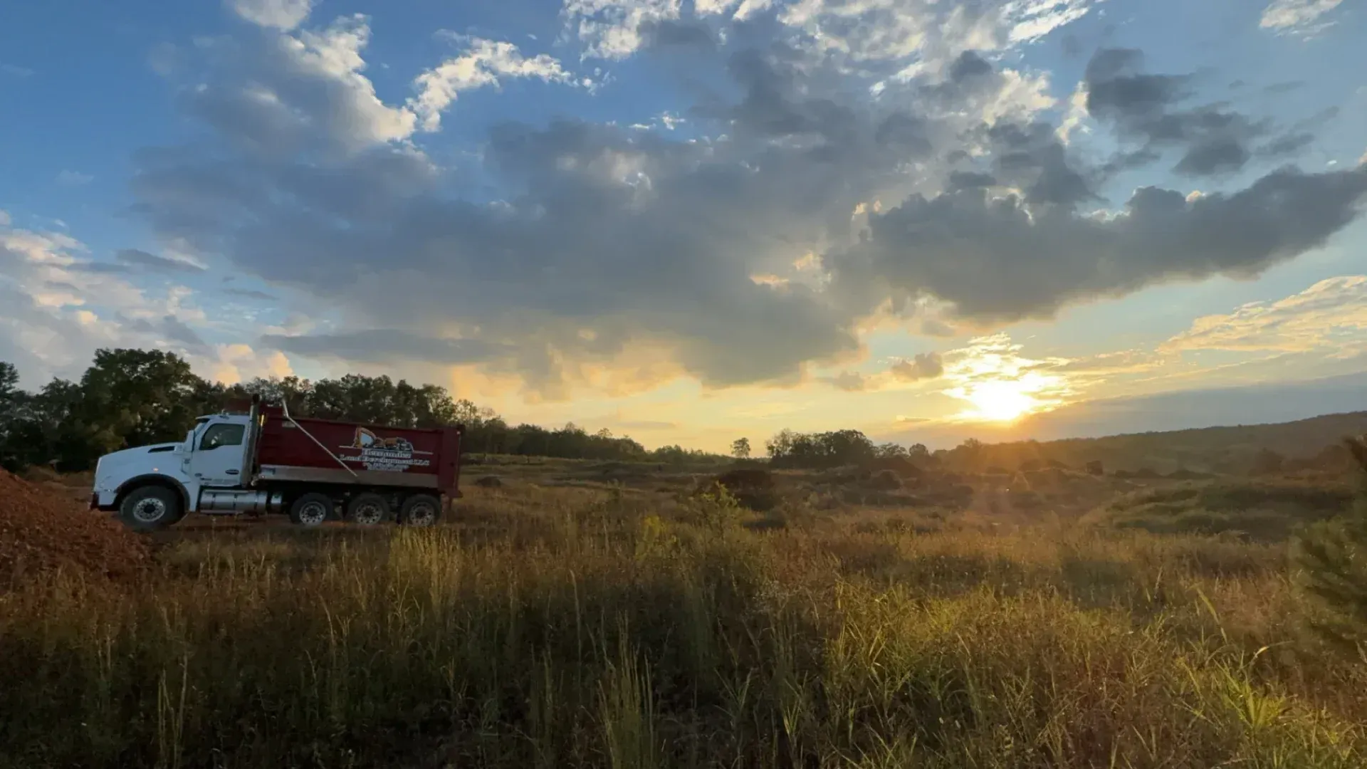 A dump truck is parked in a field at sunset.