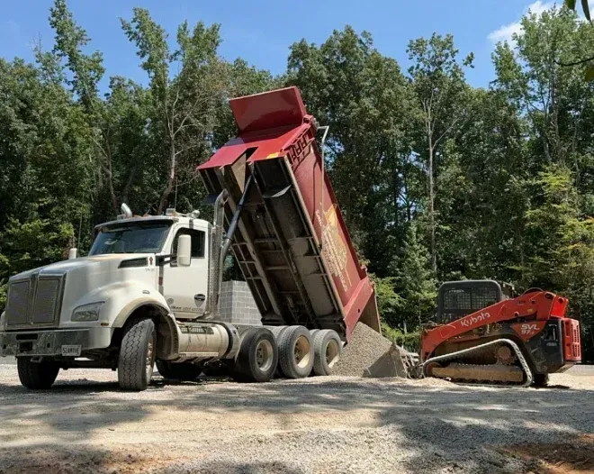 A dump truck is being loaded with gravel next to a bulldozer.
