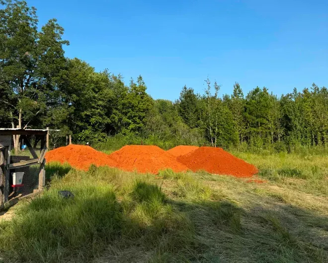 A pile of red dirt is sitting in the middle of a grassy field.