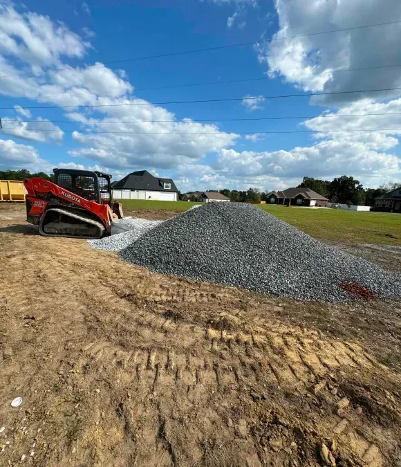 A bulldozer is moving a pile of gravel in a dirt field.