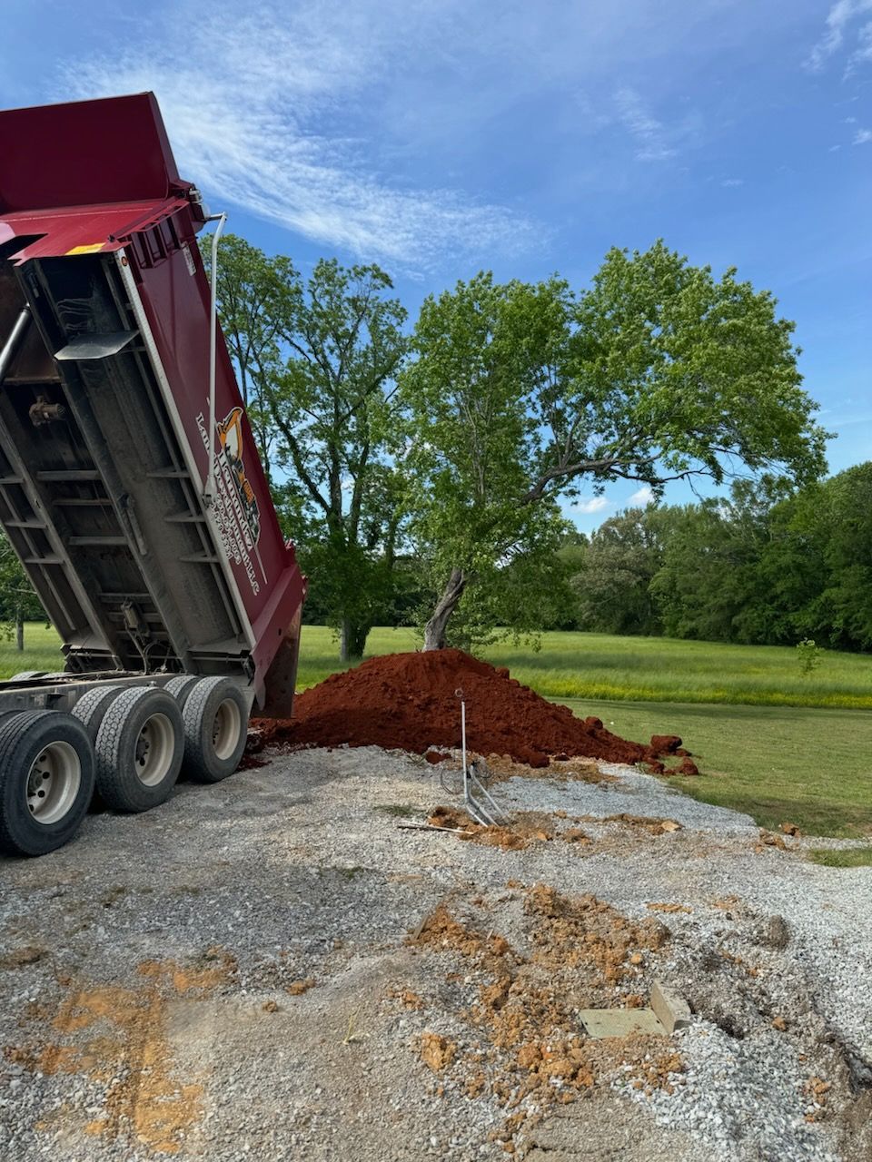 A dump truck is dumping dirt into a pile of gravel.