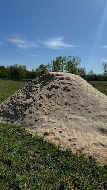 A large pile of sand is sitting in the middle of a grassy field.