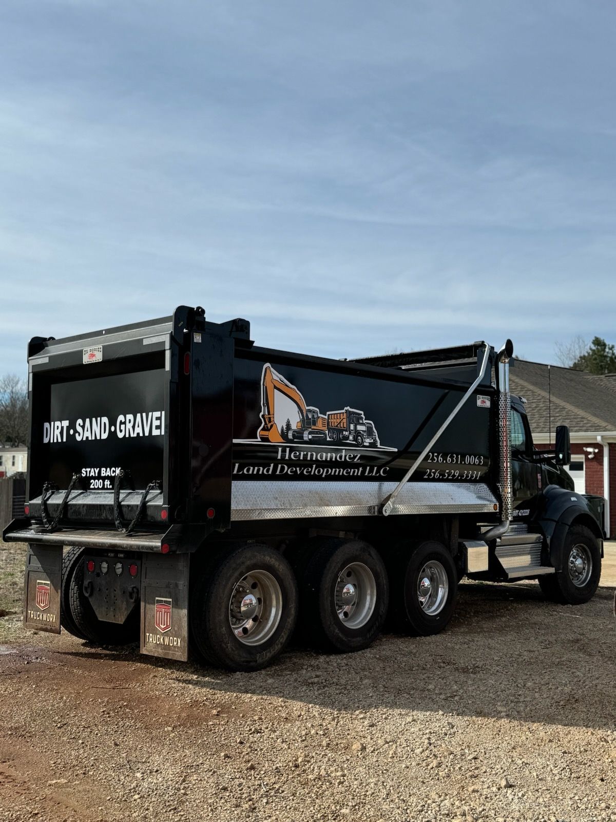 A dump truck is parked in a gravel lot in front of a house.