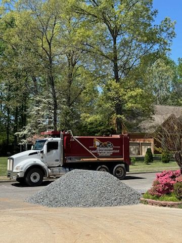 A dump truck is parked in a driveway next to a pile of gravel.