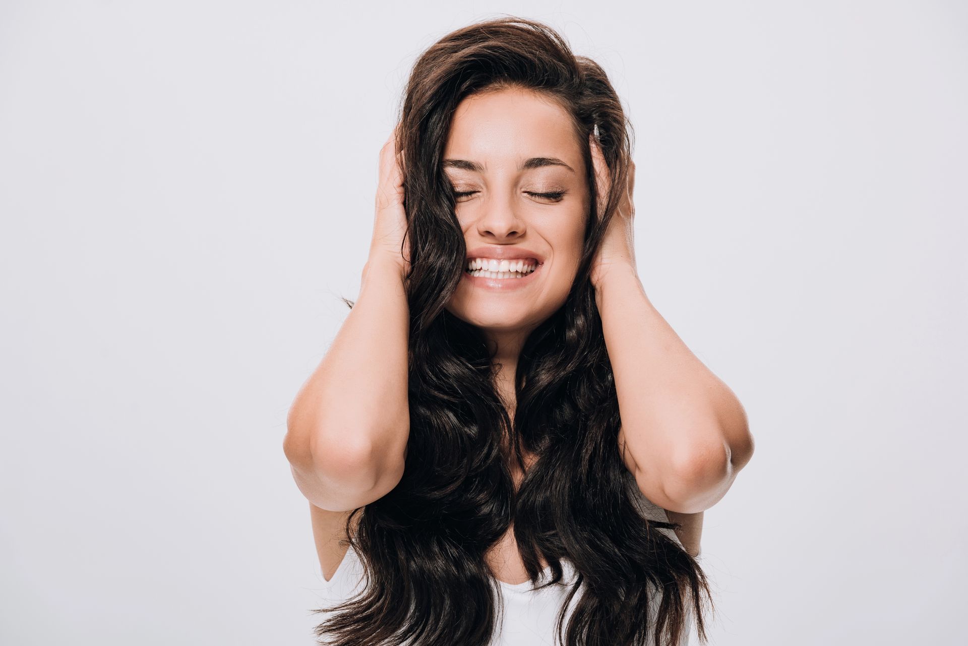 Donna sorridente con lunghi capelli scuri che si tiene la testa tra le mani, su uno sfondo chiaro.