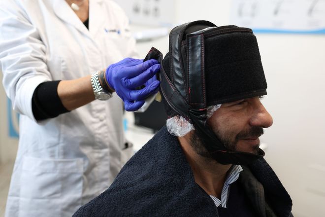 Operatrice HairAid con guanti che applica un casco tricologico terapeutico sul paziente per il trattamento non chirurgico