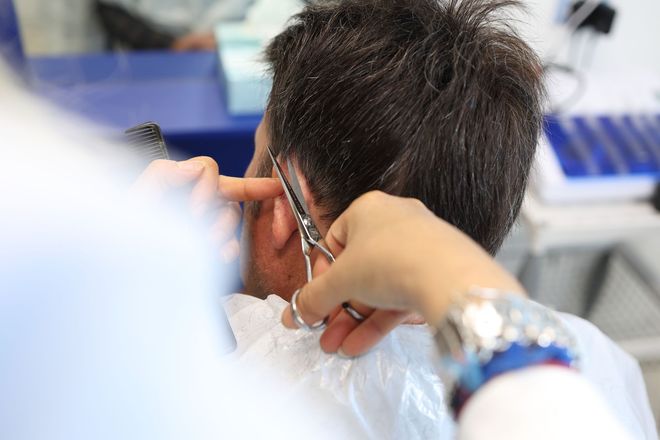 Tecnico HairAid che taglia con forbici professionali i capelli di un paziente nella zona laterale del cuoio capelluto