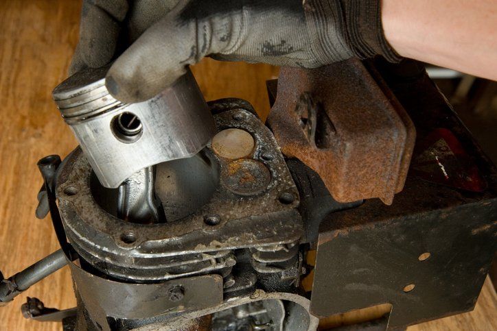 a person is holding a piston on top of a lawn mower engine .