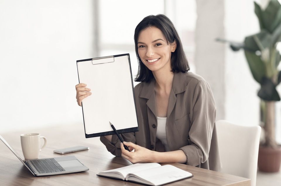 Smiling woman showing white clipboard at office