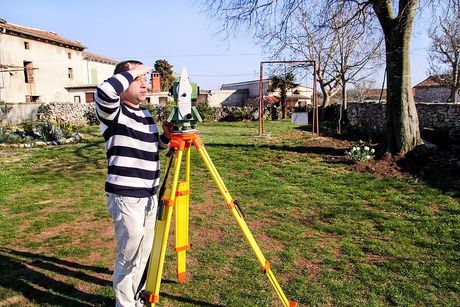 A man in a striped shirt is standing in a grassy field with a tripod.
