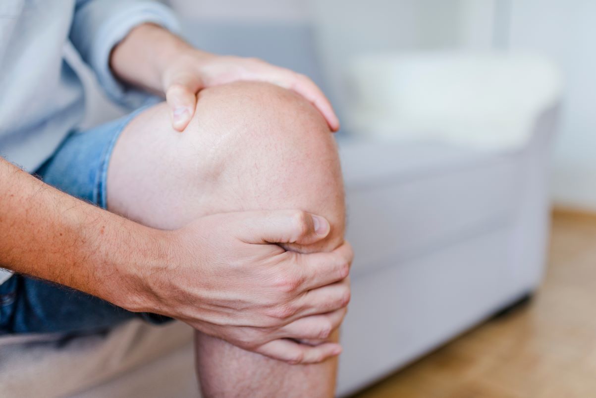 a person is sitting on a couch holding their knee in pain .