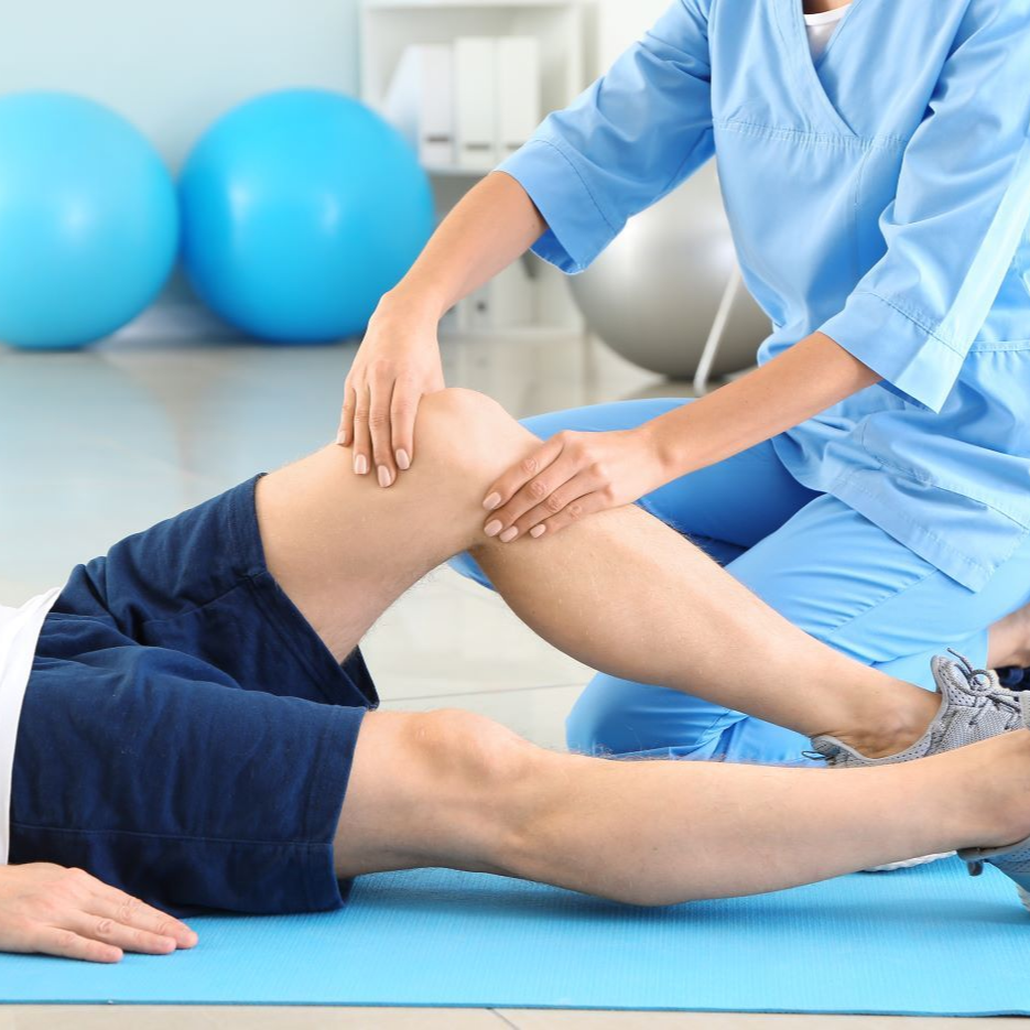 Physical therapist examines a patient's knee; both are in a therapy room with exercise balls near Fort Bragg, NC.