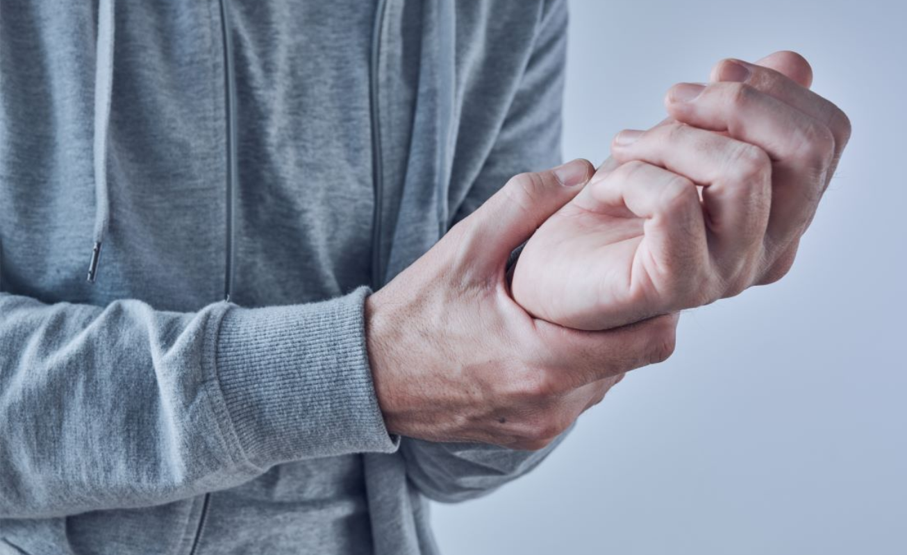 Person in gray hoodie holds wrist, possibly in pain near Fort Bragg, NC.