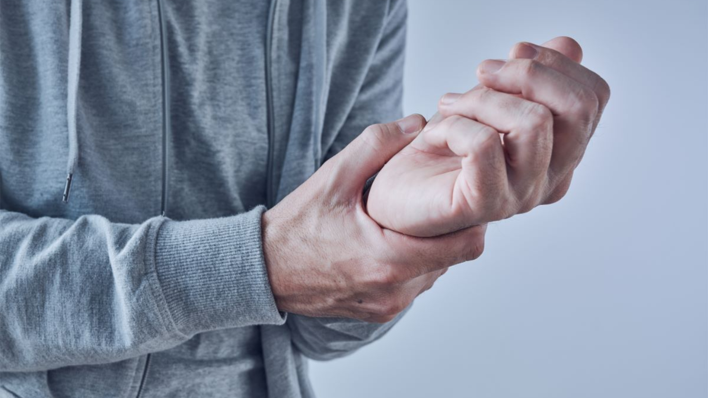 Person in gray hoodie holds wrist, possibly in pain in Fayetteville, NC.