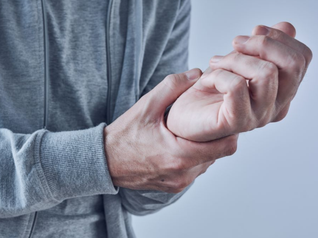 Person in gray hoodie holds wrist, possibly in pain in Hope Mills, NC.