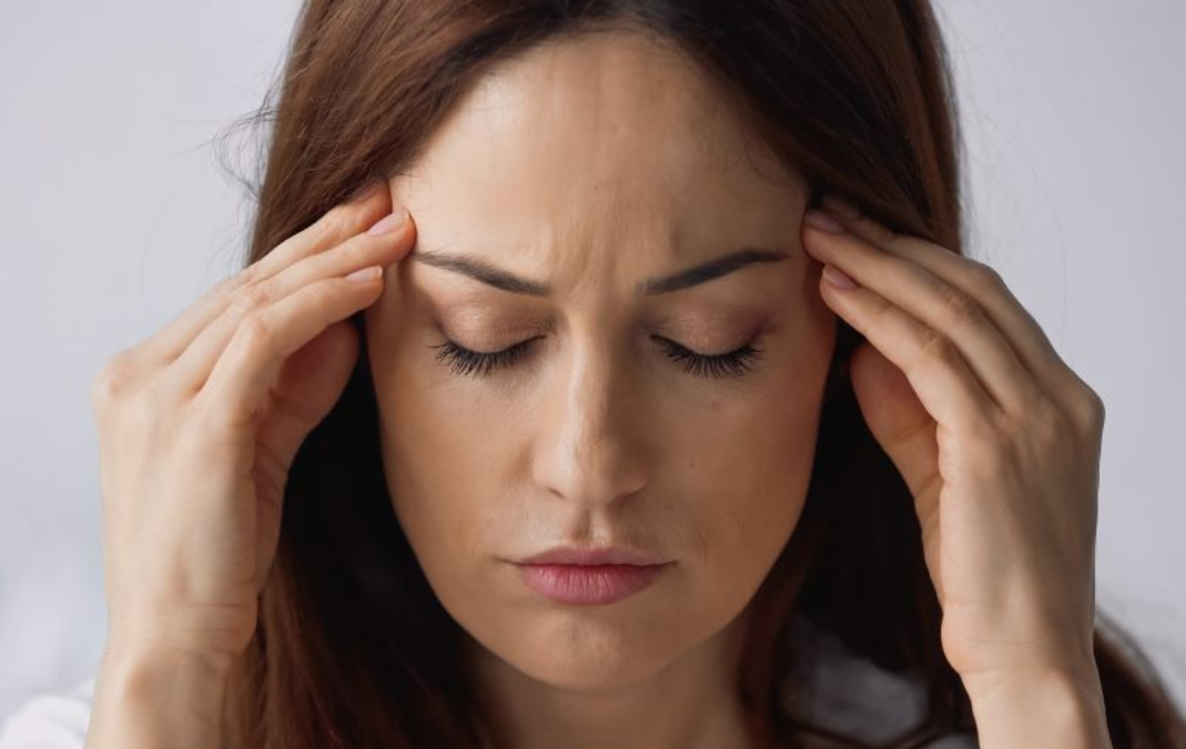 Woman with closed eyes, holding temples, appears to be in pain or experiencing headache in near Fort Bragg, NC.