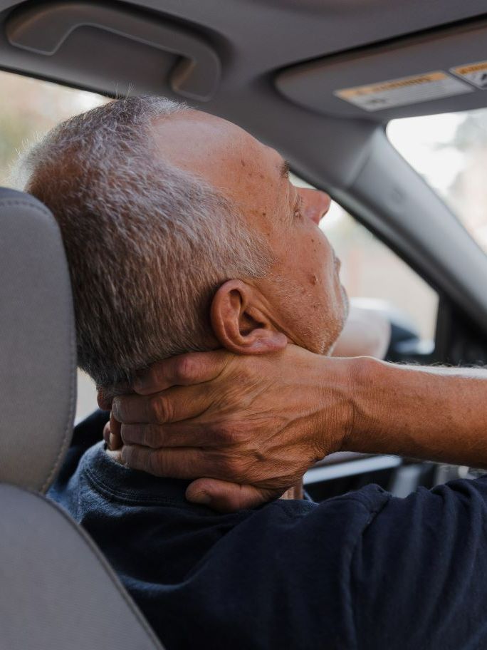 a man is holding his neck in pain while driving a car .