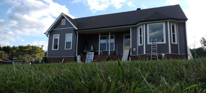 Gray house with a dark roof and white trim, seen low from the grass under a partly cloudy sky