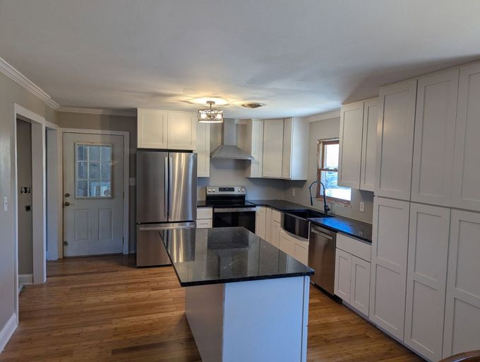 Bright open kitchen and living room with white cabinets, island, wood floors, and large windows