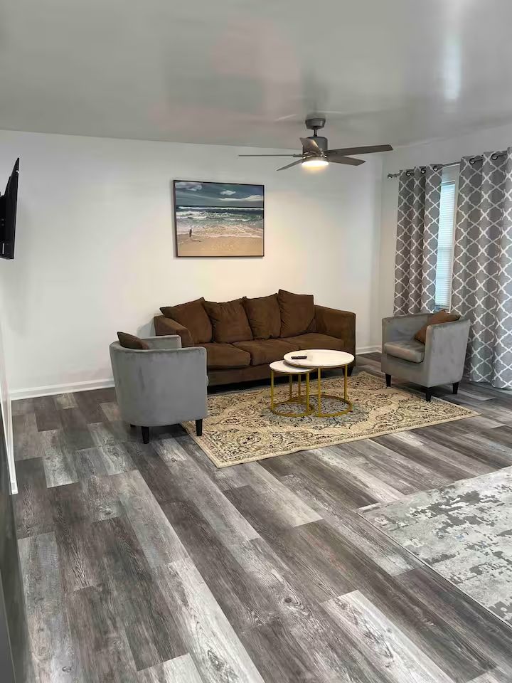 A living room with a couch , chairs , a table and a ceiling fan.