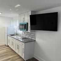 A kitchen with white cabinets , a refrigerator , a microwave , and a flat screen tv.