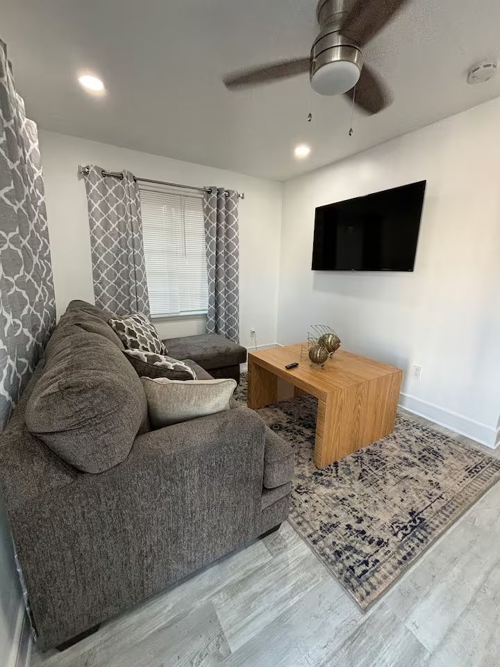 A living room with a couch , chair , coffee table , television and ceiling fan.