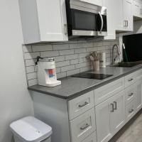 A kitchen with white cabinets , a microwave , a sink , and a trash can.