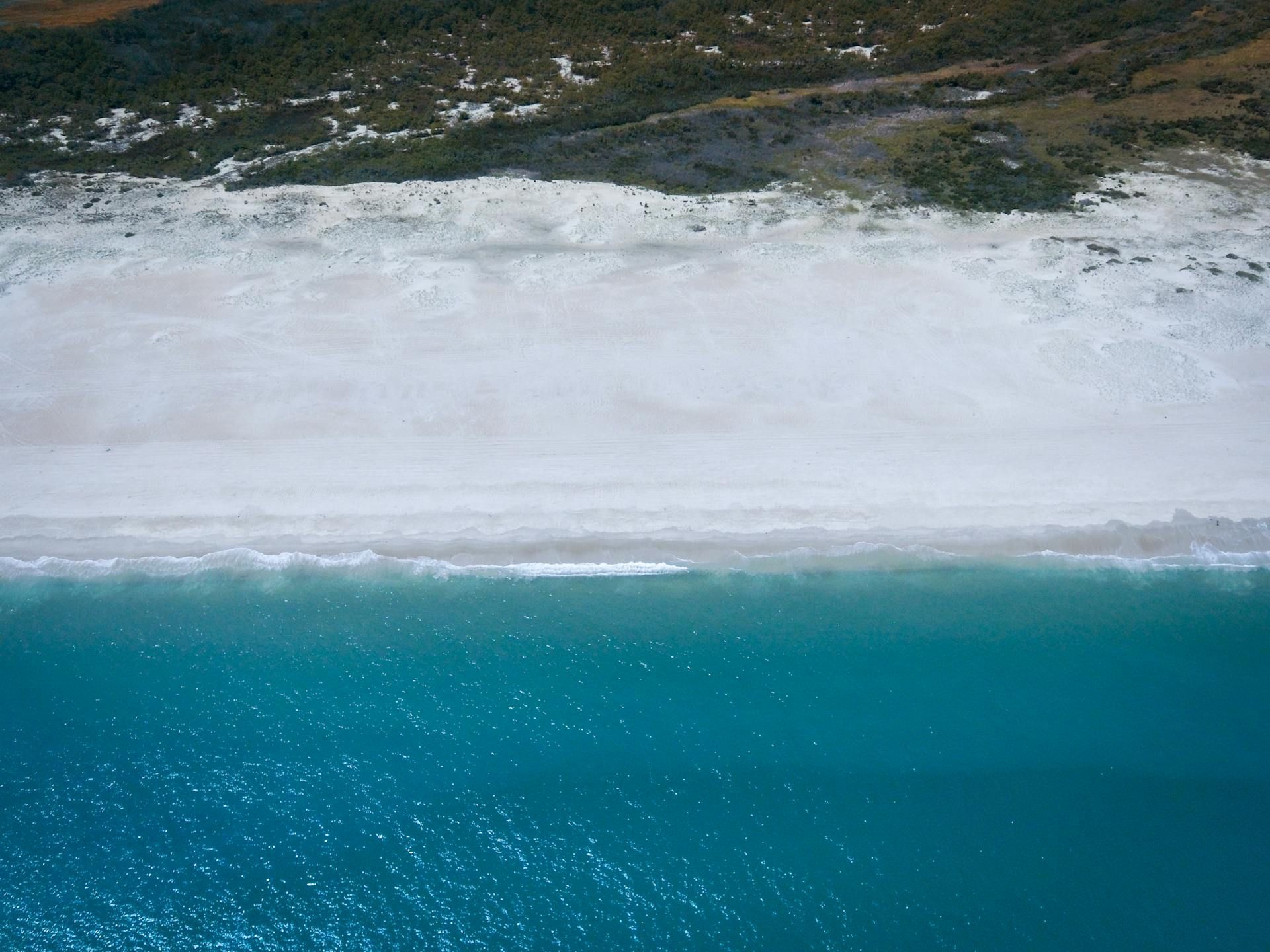 An aerial view of a beach with turquoise water and white sand.