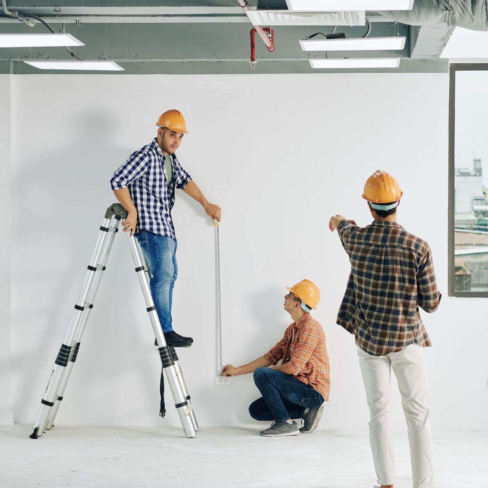 a man on a ladder measuring a wall with a tape measure