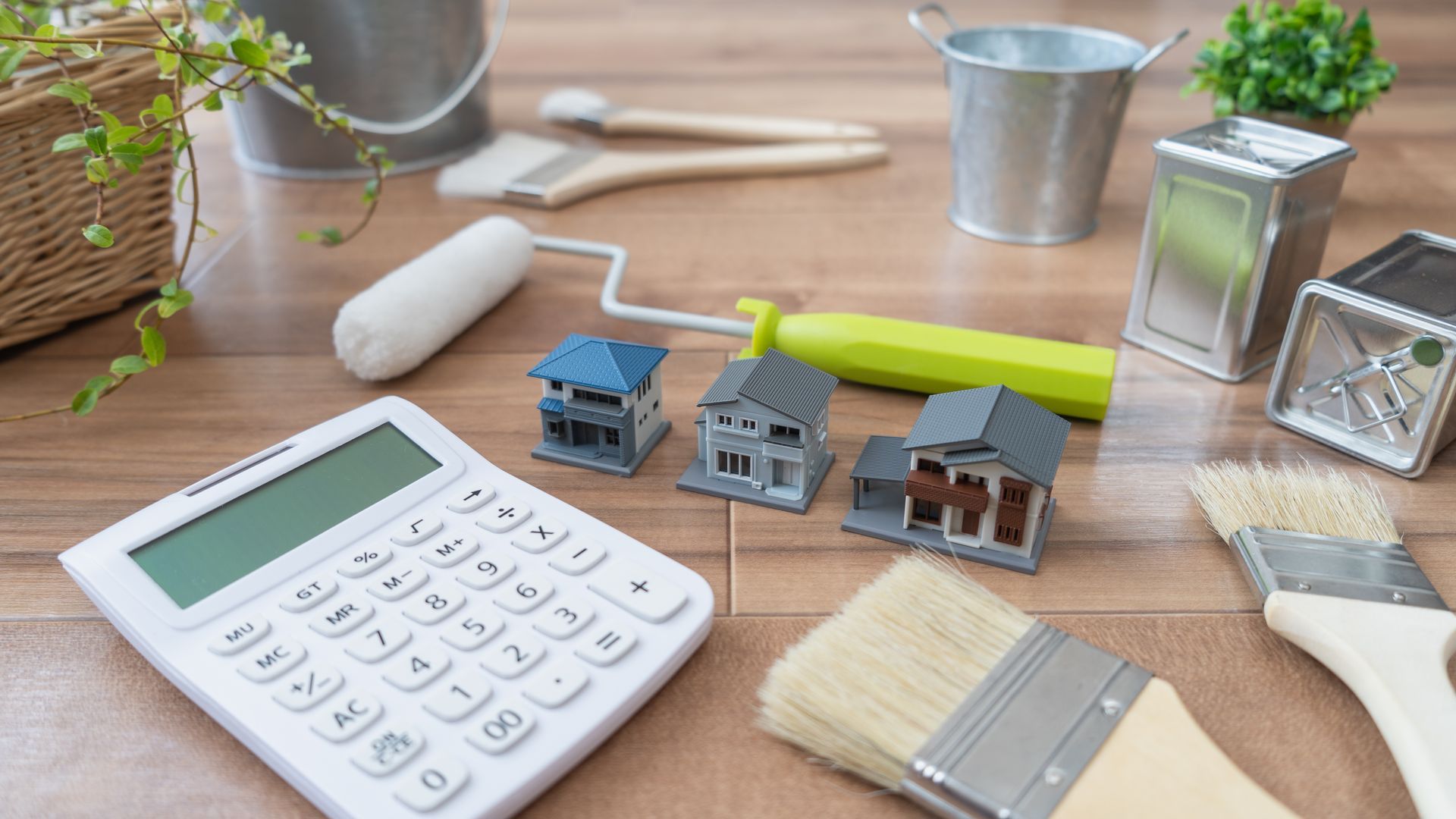 a calculator, brushes, paint rollers, and miniature houses are on a wooden table
