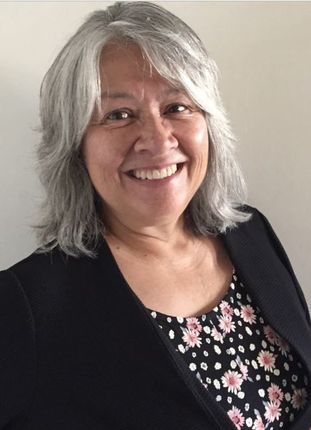 Woman with gray hair smiling, wearing a floral top and black jacket.