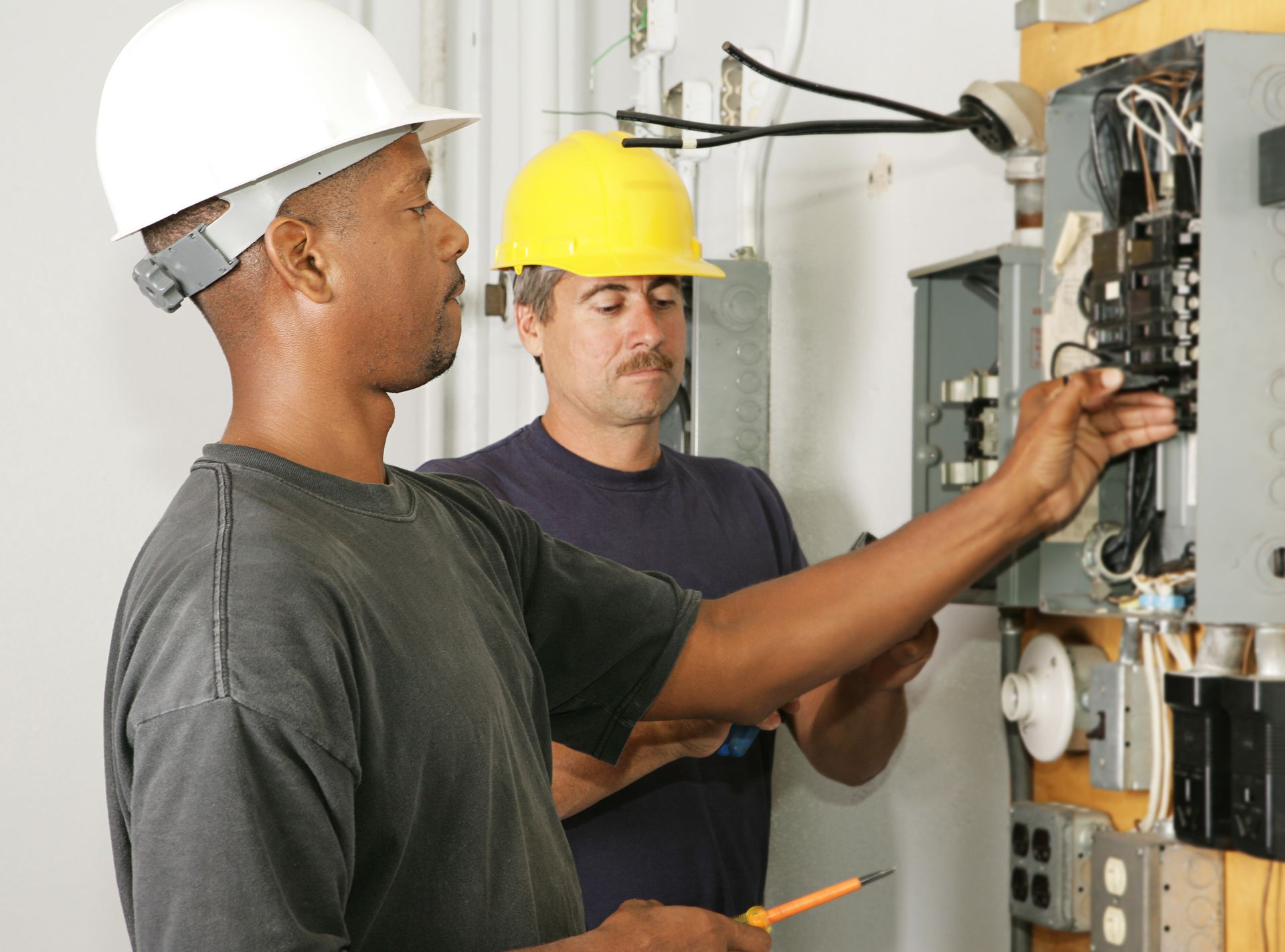Two electricians inspecting a circuit breaker panel for a professional electrical contractor.