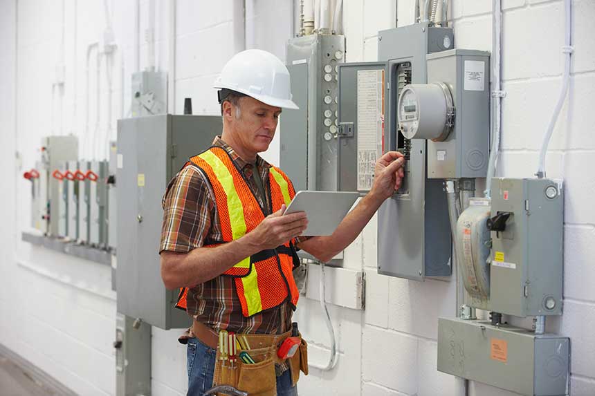 Electrician Repairing Fuse Box and Holding Digital Tablet — Richmond, VA — Beckstoffer Welsh Inc.