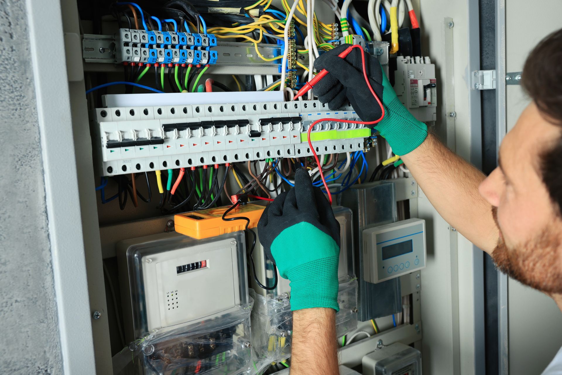 Electrician in gloves wiring a panel with bundled colored cables.