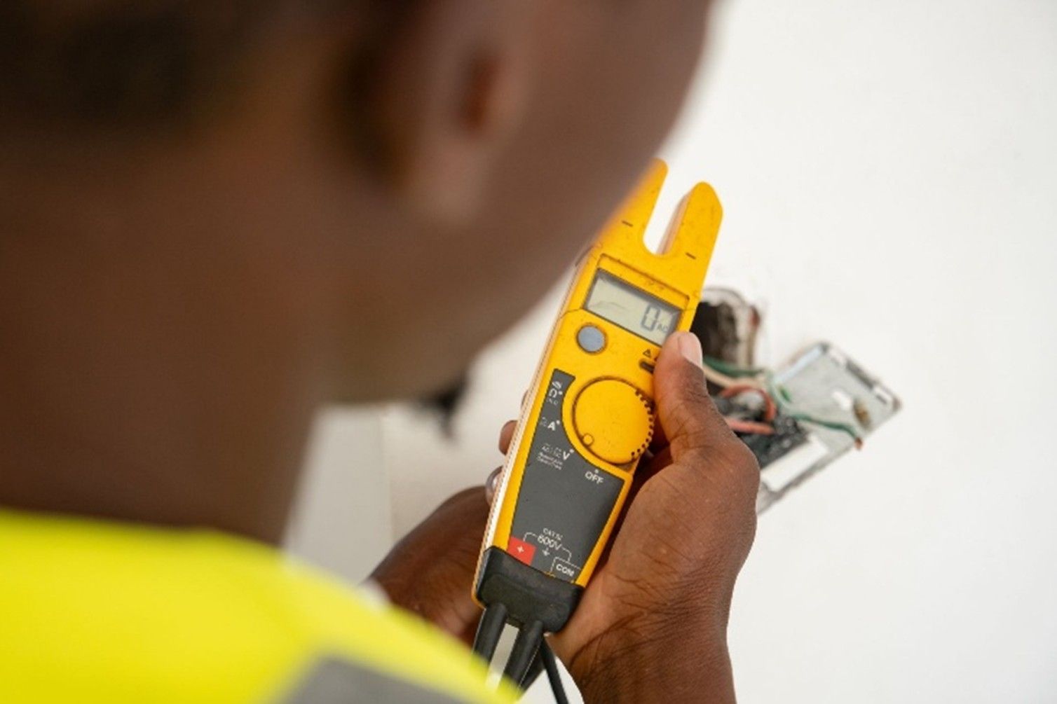An electrician using a voltage tester to check wiring inside an open wall socket during repair An electrician using a voltage tester to check wiring inside an open wall socket during repair