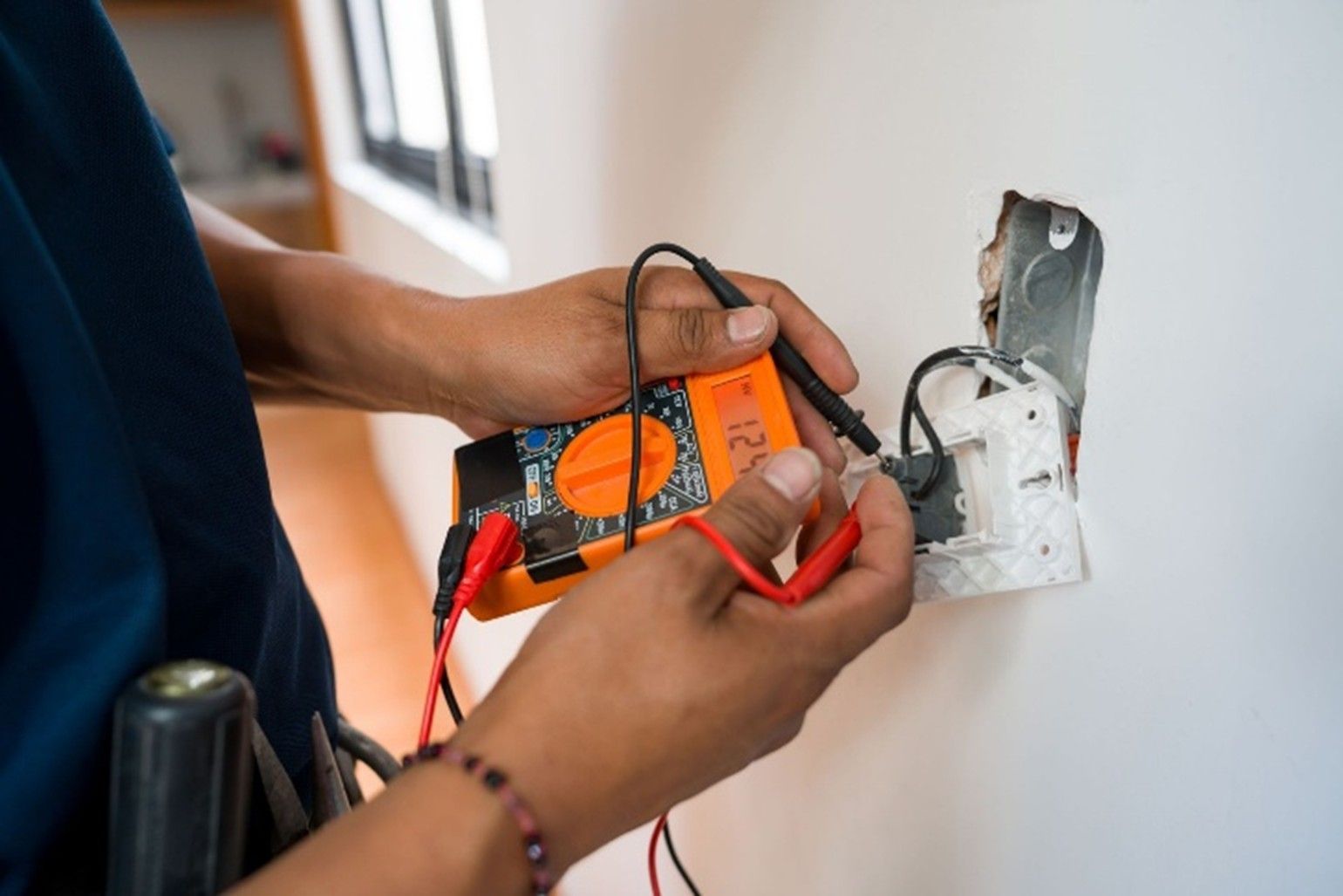 An electrician using a digital multimeter to test wiring inside a wall socket during repair work An electrician using a digital multimeter to test wiring inside a wall socket during repair work