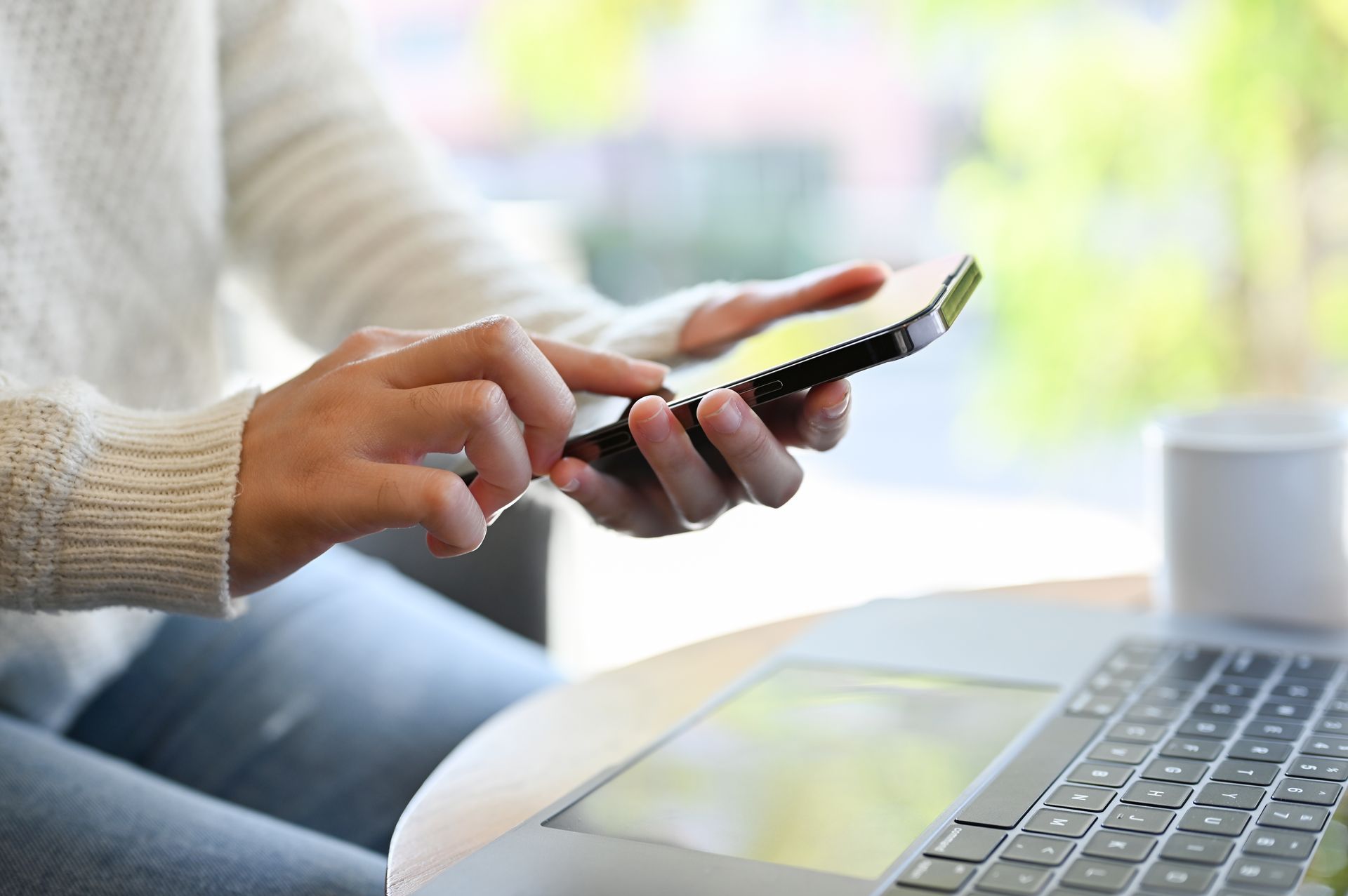 Person using a smartphone near a laptop, indoors.