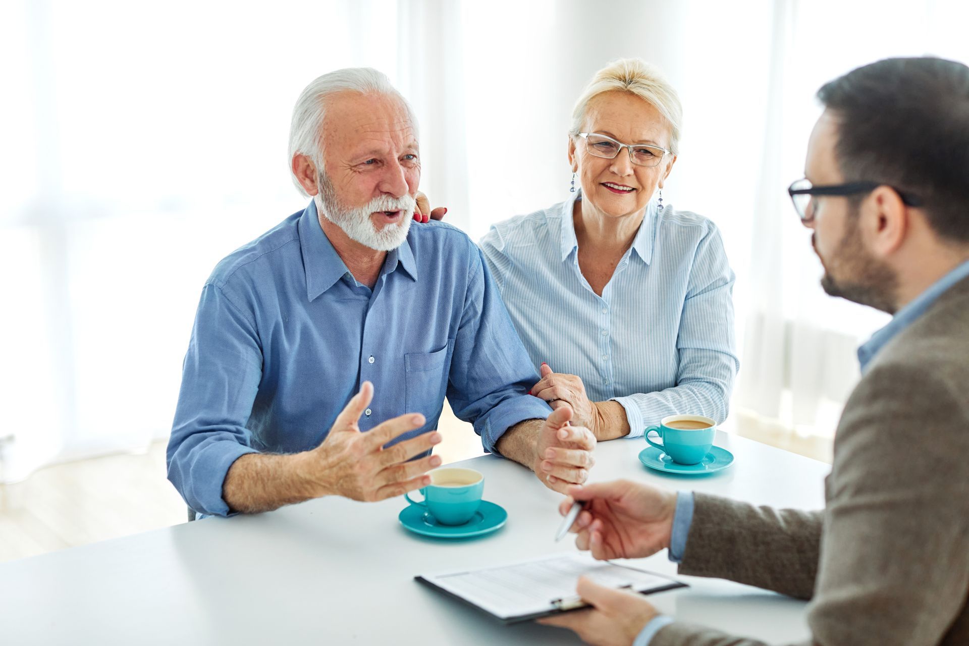 Older couple talking to a professional; table with coffee, paperwork.