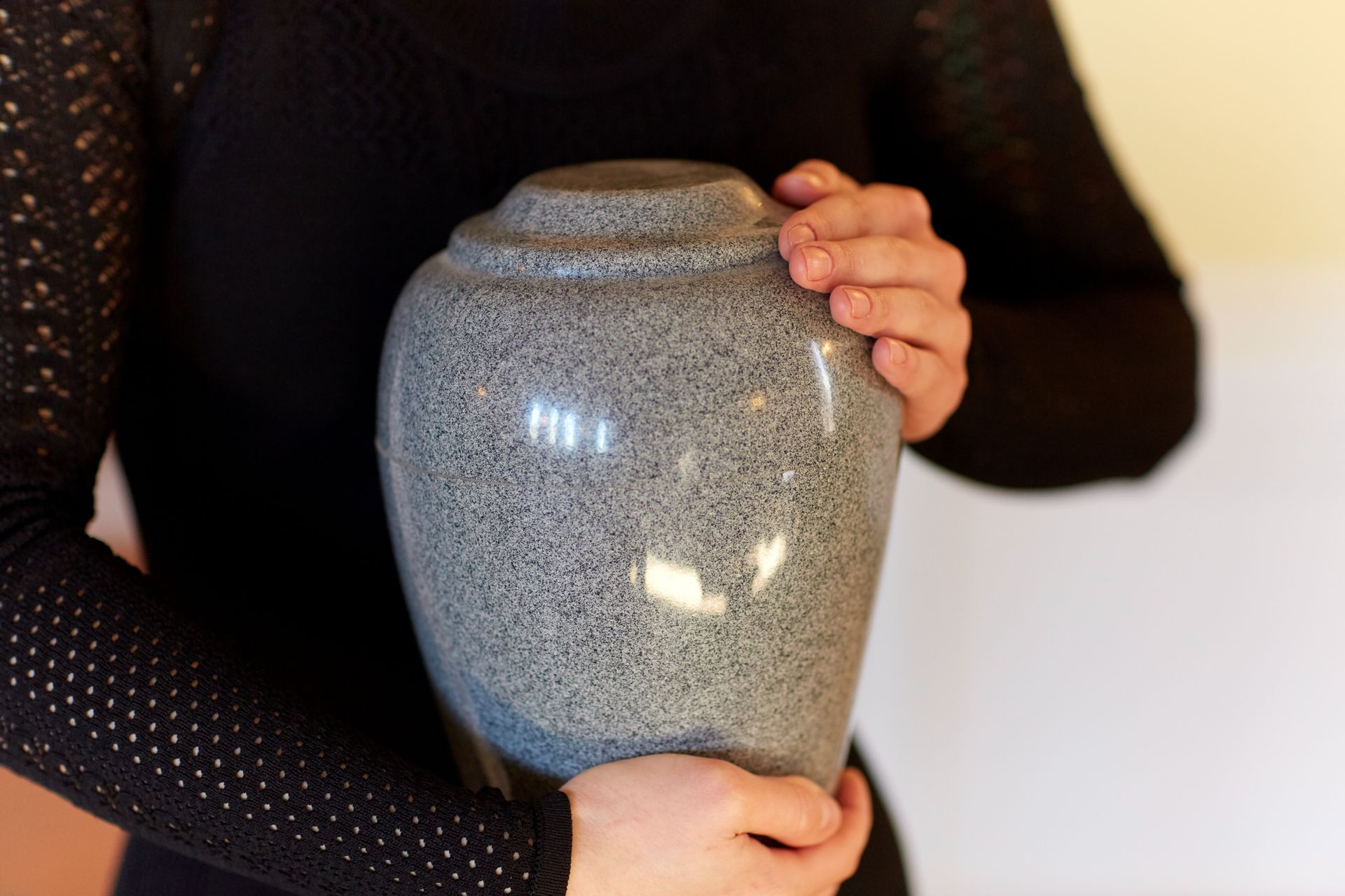 Person in black clothing holding a speckled gray urn.