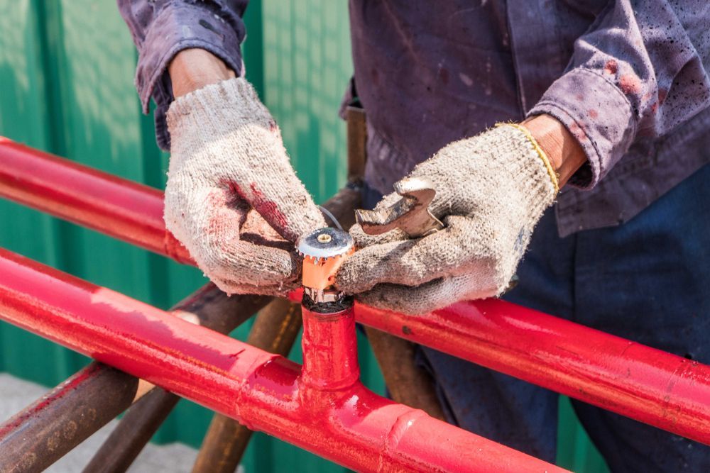 Person Wearing Gloves Assembling Red Painted Metal Pipes — Quik Fire Electrical in Kelmscott, WA