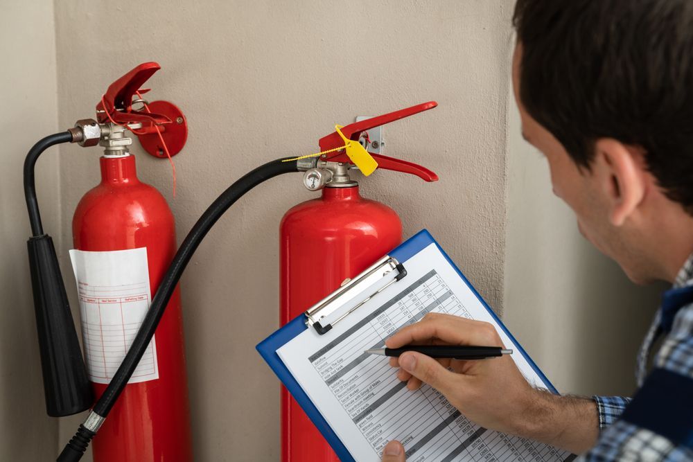Man Inspecting Fire Extinguishers, Writing On A Checklist — Quik Fire Electrical in Kelmscott, WA