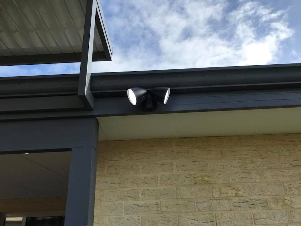 Two Black Outdoor Lights Mounted Under a Roof Eave Above a Beige Brick Wall — Quik Fire Electrical in Kelmscott, WA