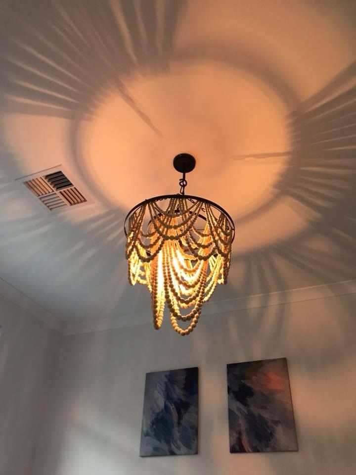 A chandelier with beaded layers casts shadows on the ceiling, beneath abstract art on a white wall.— Quik Fire Electrical in Kelmscott, WA