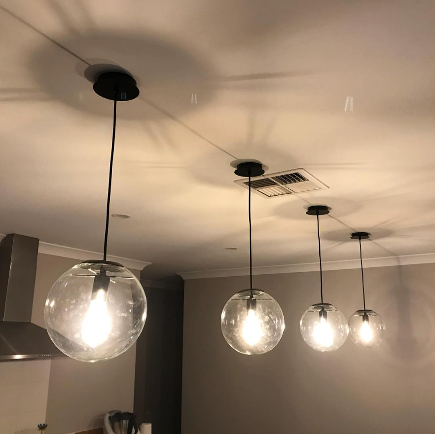 Four pendant lights with clear glass globes hanging from a white ceiling, lit.— Quik Fire Electrical in Kelmscott, WA