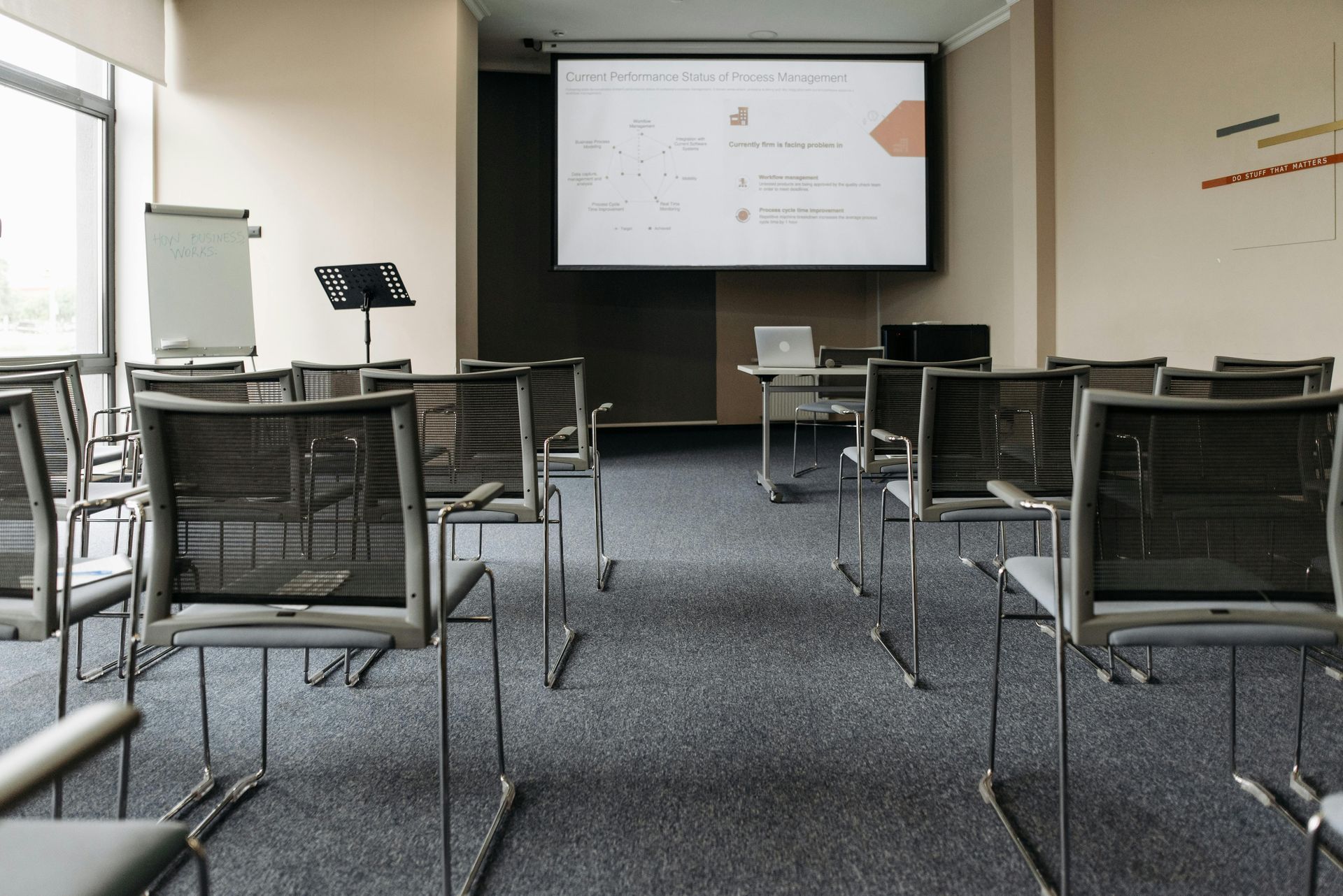 Empty conference room with rows of chairs facing a projection screen displaying a presentation.