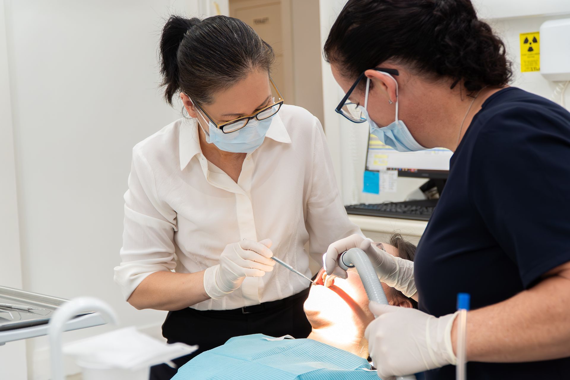 Two women are working on a patient 's teeth in a dental office.