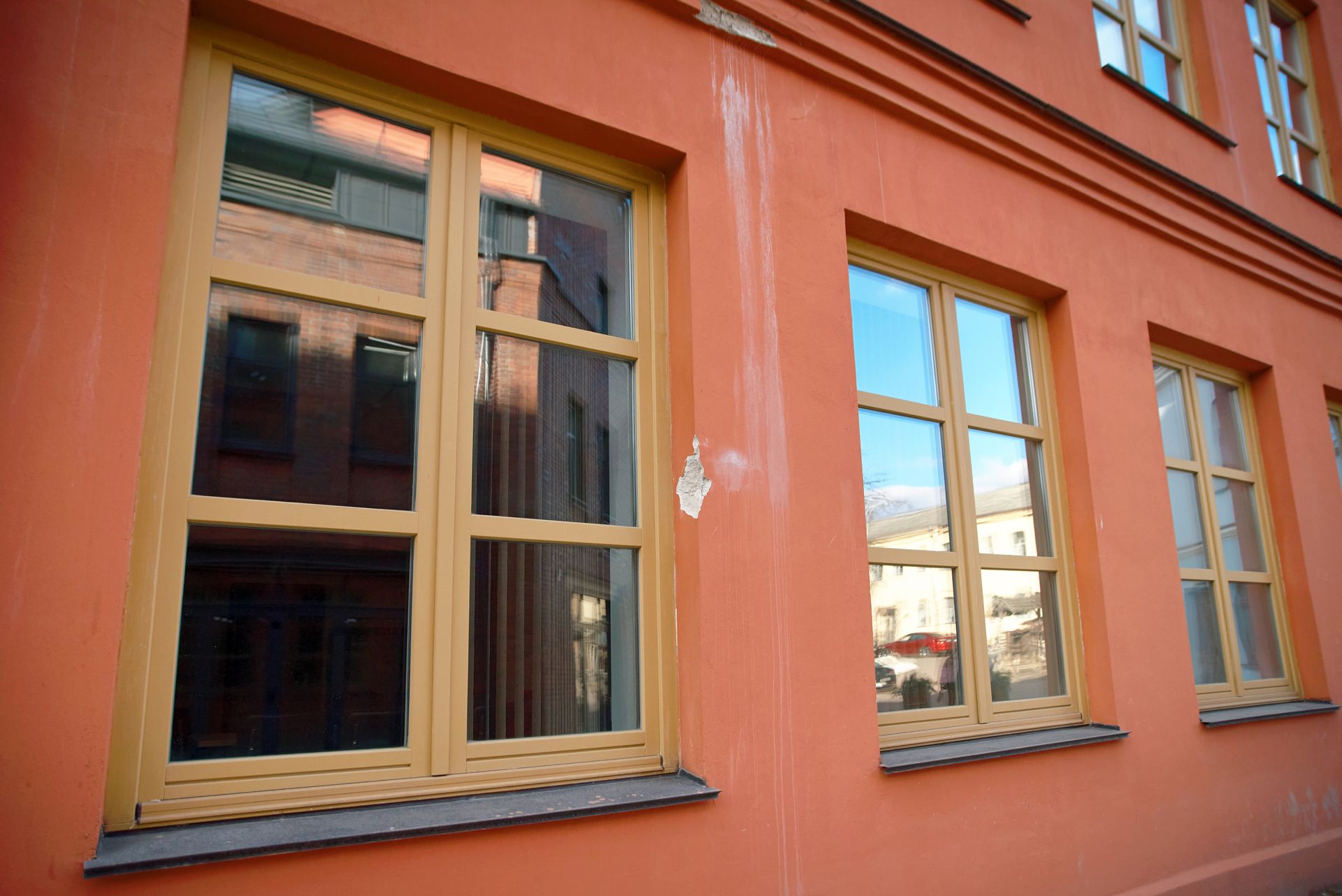 Orange building facade with multiple windows, reflecting the sky and surrounding buildings.