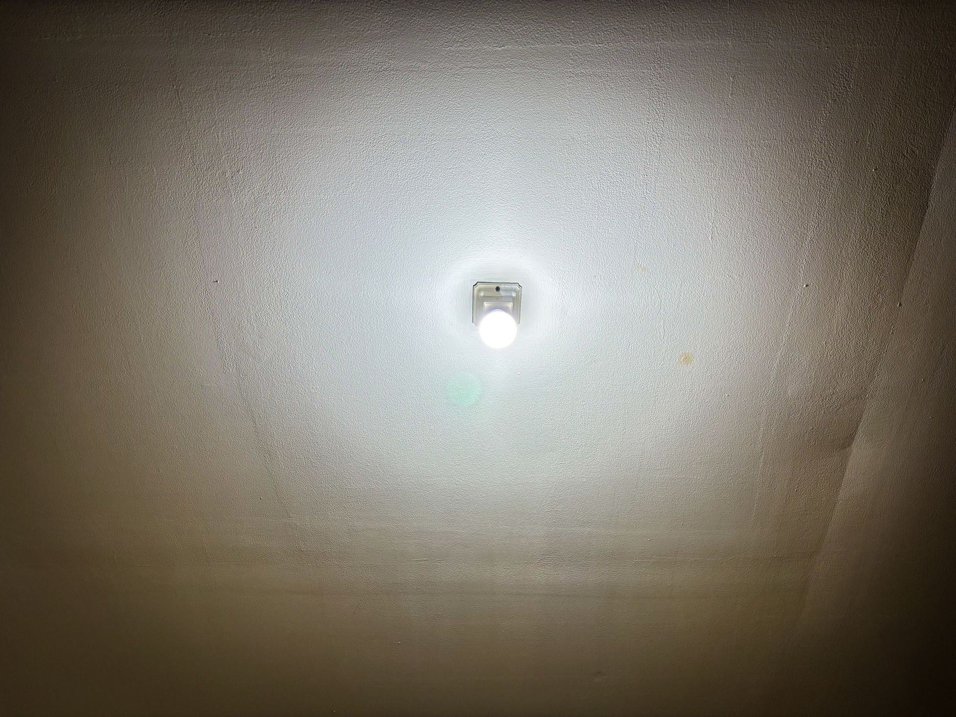 Bright ceiling light casting a large, circular glow on a textured, off-white ceiling.