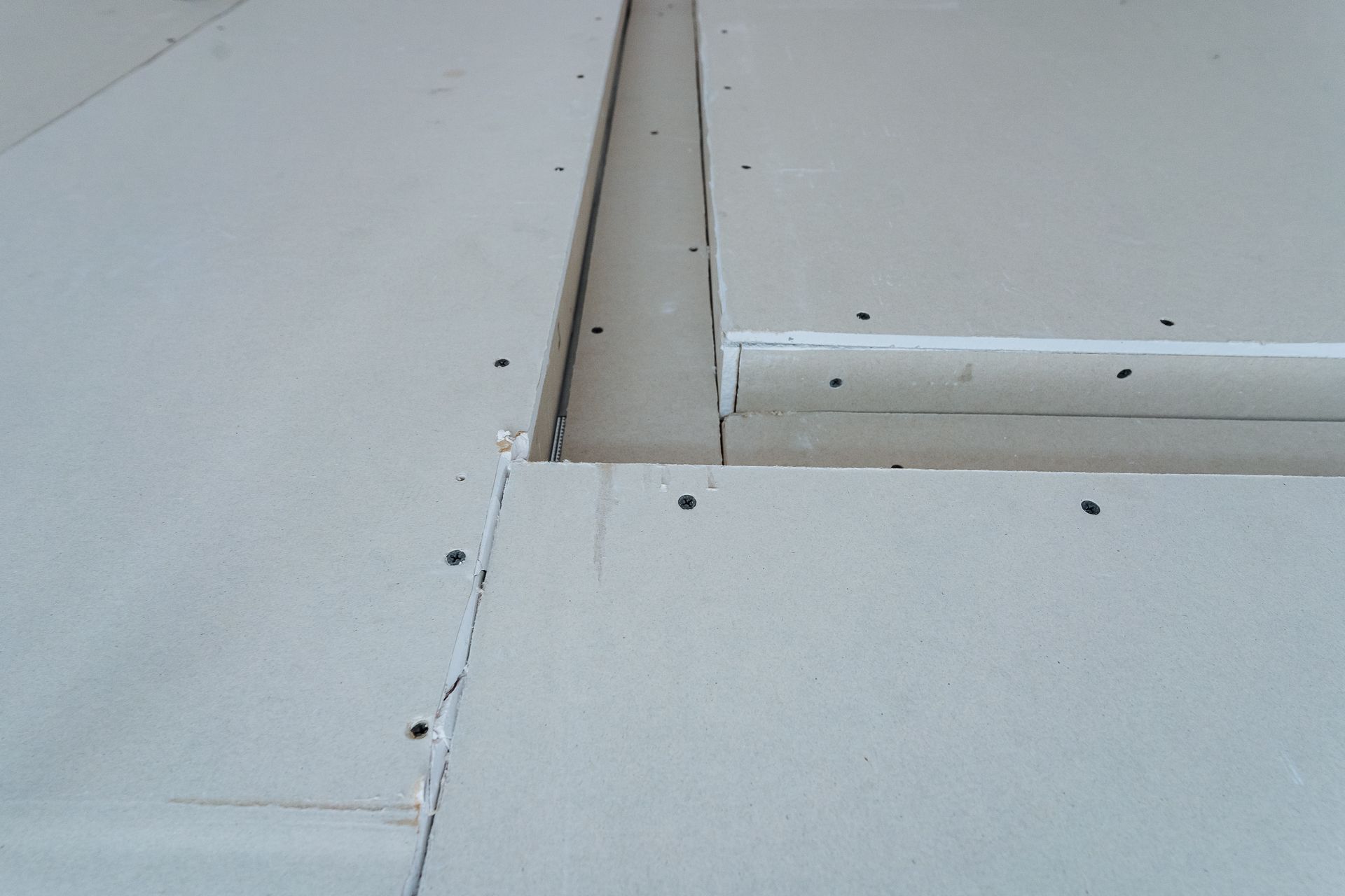 Drywall installation with visible joints, screws, and cracks, inside a building.